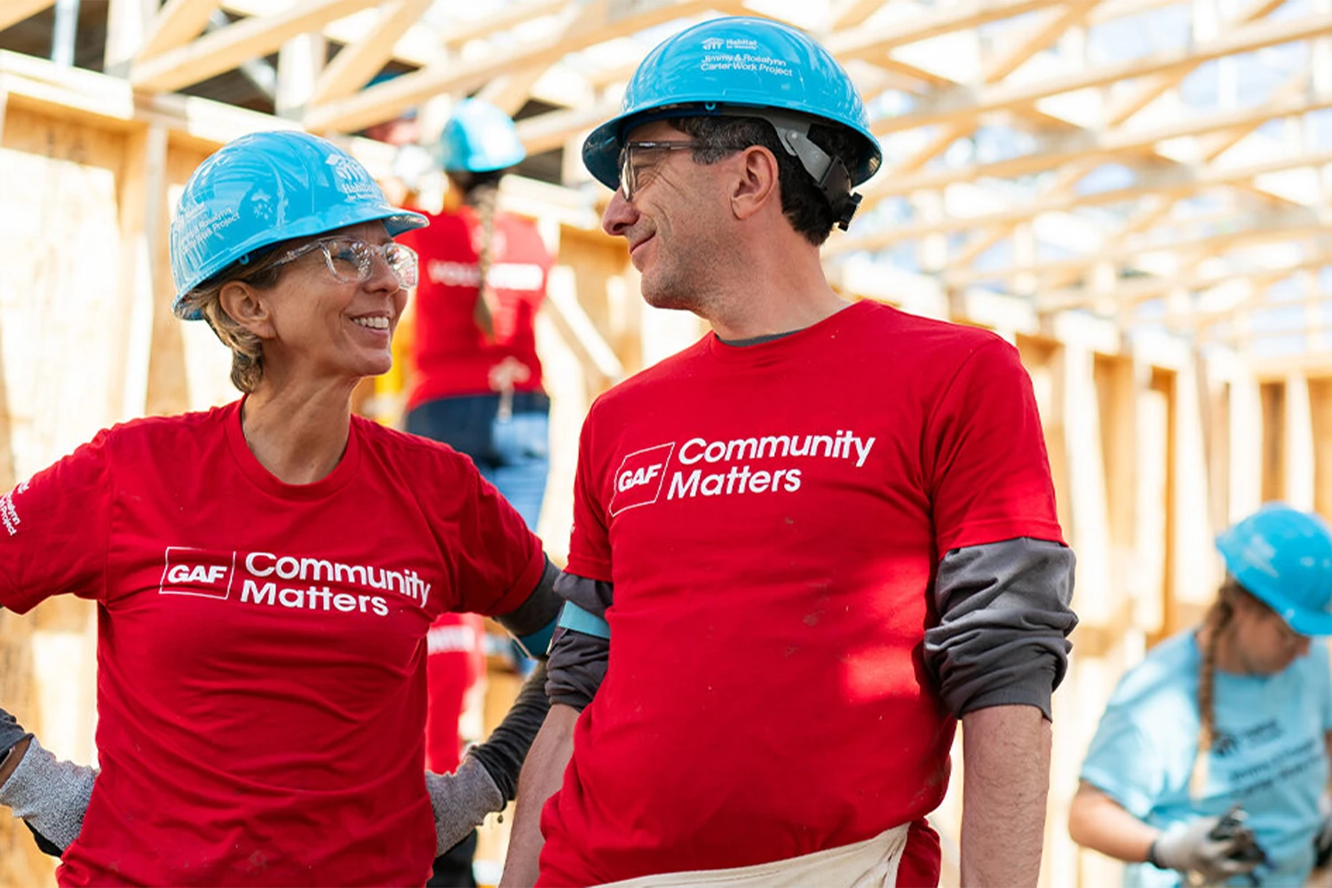 Two GAF volunteers in blue hard hats smiling at each other.