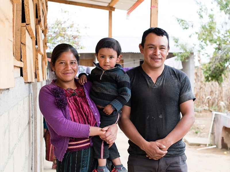 A man and a woman smiling, standing with a small child outside a building.