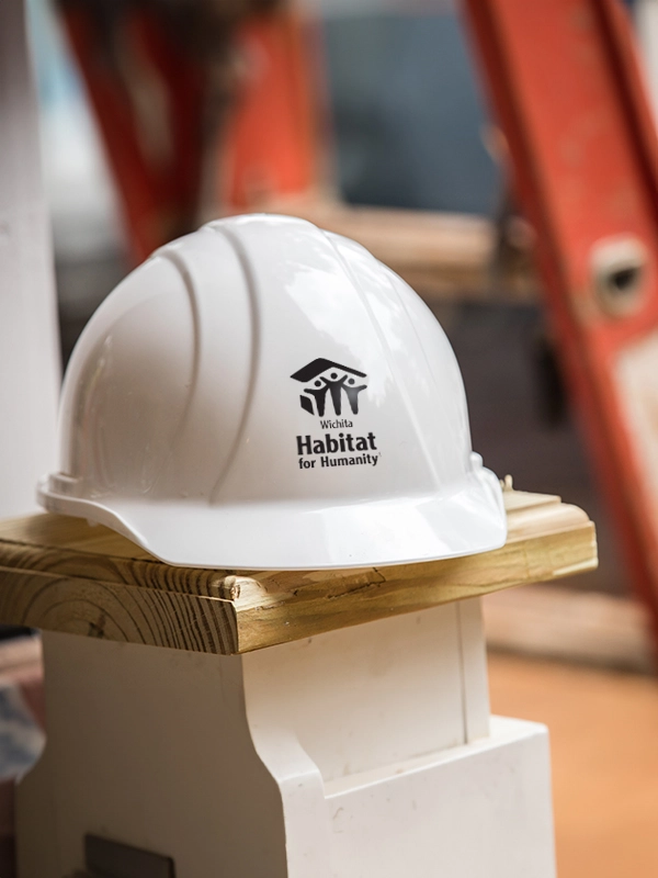 White hard hat with the Wichita Habitat for Humanity logo sitting on wooden construction material.