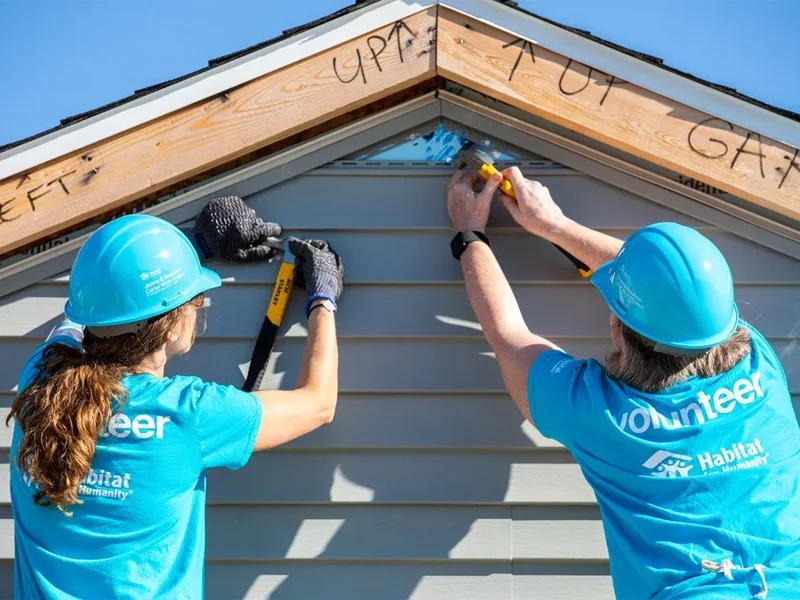 Two Habitat for Humanity volunteers install siding on a house under construction.