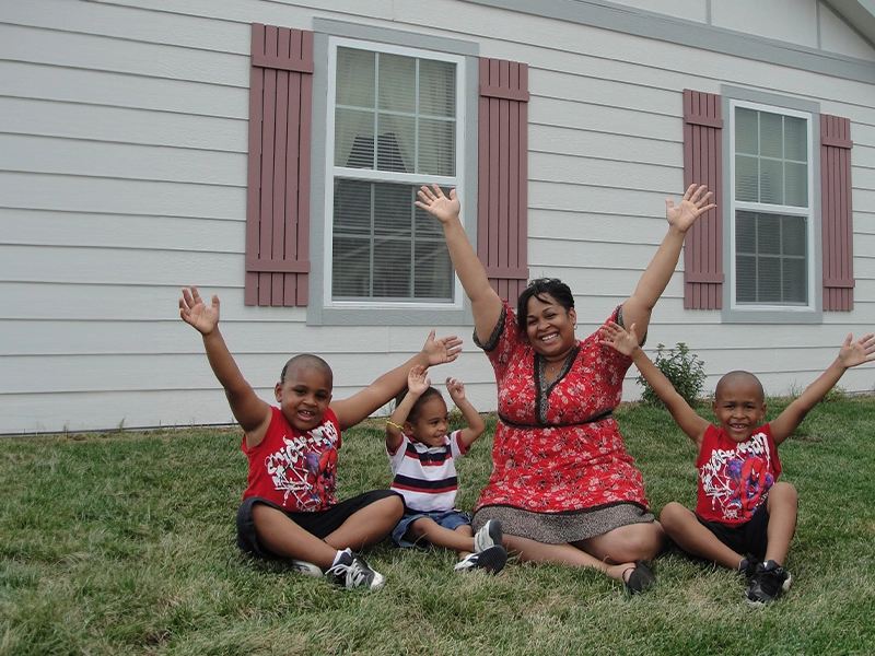A Habitat for Humanity homeowner and her three children celebrating on the front lawn of their new home.