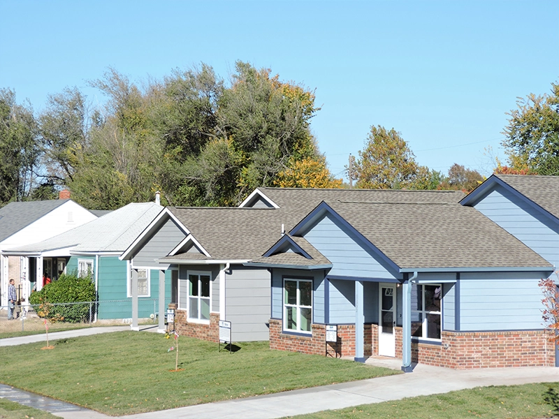 Row of newly constructed single-story homes with blue and gray siding and red brick foundations.