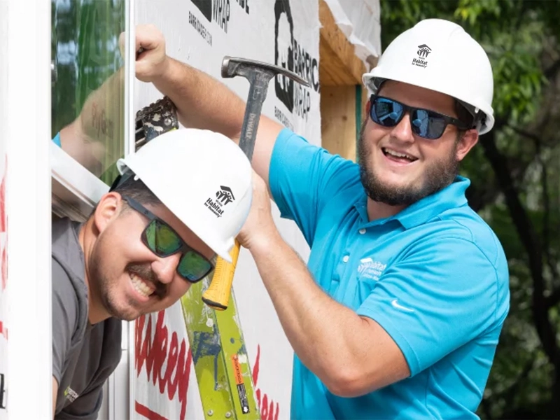 Two volunteers smiling together while one is holding a hammer.
