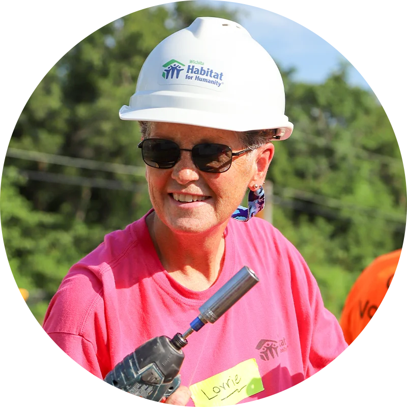 Close-up of a smiling volunteer named Lorrie wearing a hard hat and holding a drill.